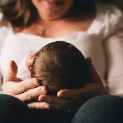 Dłoń matki trzymająca główkę noworodka.