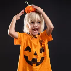 Chłopiec w pomarańczowej koszulce z namalowaną buźką dyni i mini dynią na głowie. Idealny pomysł, jak zrobić strój dyni z bibuły na Halloween!