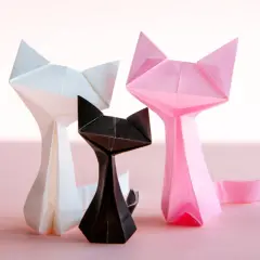 Trzy papierowe koty origami: biały, czarny i różowy, na jasnoróżowym tle.