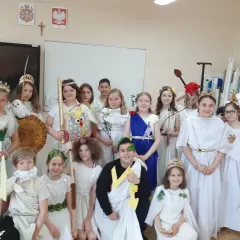 Dzieci w strojach antycznych bogów i bogiń, jak Artemida, pozują do zdjęcia. W tle szkielet i tablica.