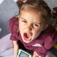 Zła mina dziecka z otwartymi ustami, trzymającego zabawkę. Czy to znak, dlaczego dziecko jest agresywne?