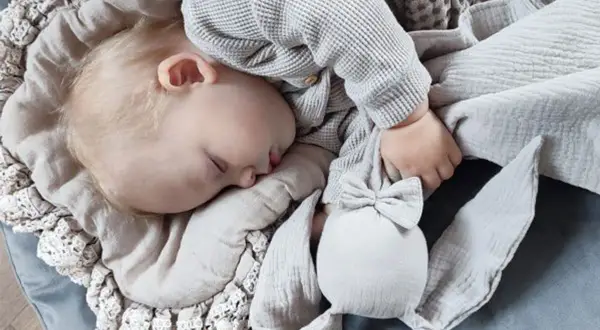 Śpiące dziecko tuli swoją pierwszą przytulankę dla niemowlaka – miękkiego króliczka.