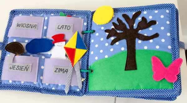 Kolorowa książka sensoryczna dla dziecka z motywami pór roku: wiosna, lato, jesień, zima. Jest tu bałwanek, latawiec, drzewo i motyl.