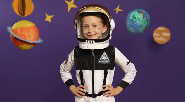 Uśmiechnięta dziewczynka w stroju kosmonauty dla dzieci, gotowa na kosmiczną przygodę wśród planet i gwiazd.