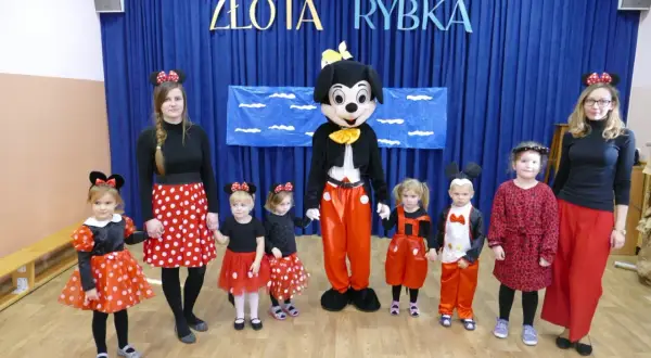 Dzieci i panie w strojach na dzień postaci z bajek, w tym Myszka Miki i Minnie, pozują do zdjęcia.