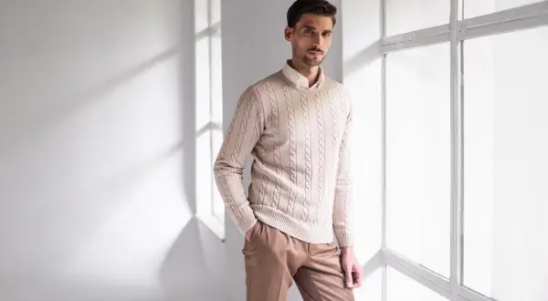 Elegancki strój na sylwestra męski: beżowy sweter z warkoczami i brązowe spodnie. Idealny na imprezę.