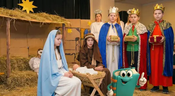 Dzieci w strojach na jasełka odgrywają scenę narodzin Jezusa. Widać Maryję, Józefa, aniołka i trzech króli z darami.