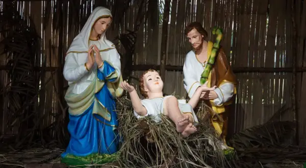 Święta Rodzina w żłóbku. Maryja w błękitnej sukni, Józef w brązowym płaszczu i biała szata Dzieciątka Jezus.