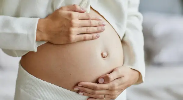 Delikatne ruchy dziecka w brzuchu, kiedy dziecko zaczyna kopać w ciąży. Dłonie matki czule obejmują ciążowy brzuszek.