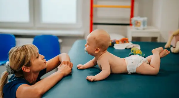 Fizjoterapeutka wspiera niemowlaka z nieprawidłowym leżeniem na brzuchu, zachęcając go do aktywności.