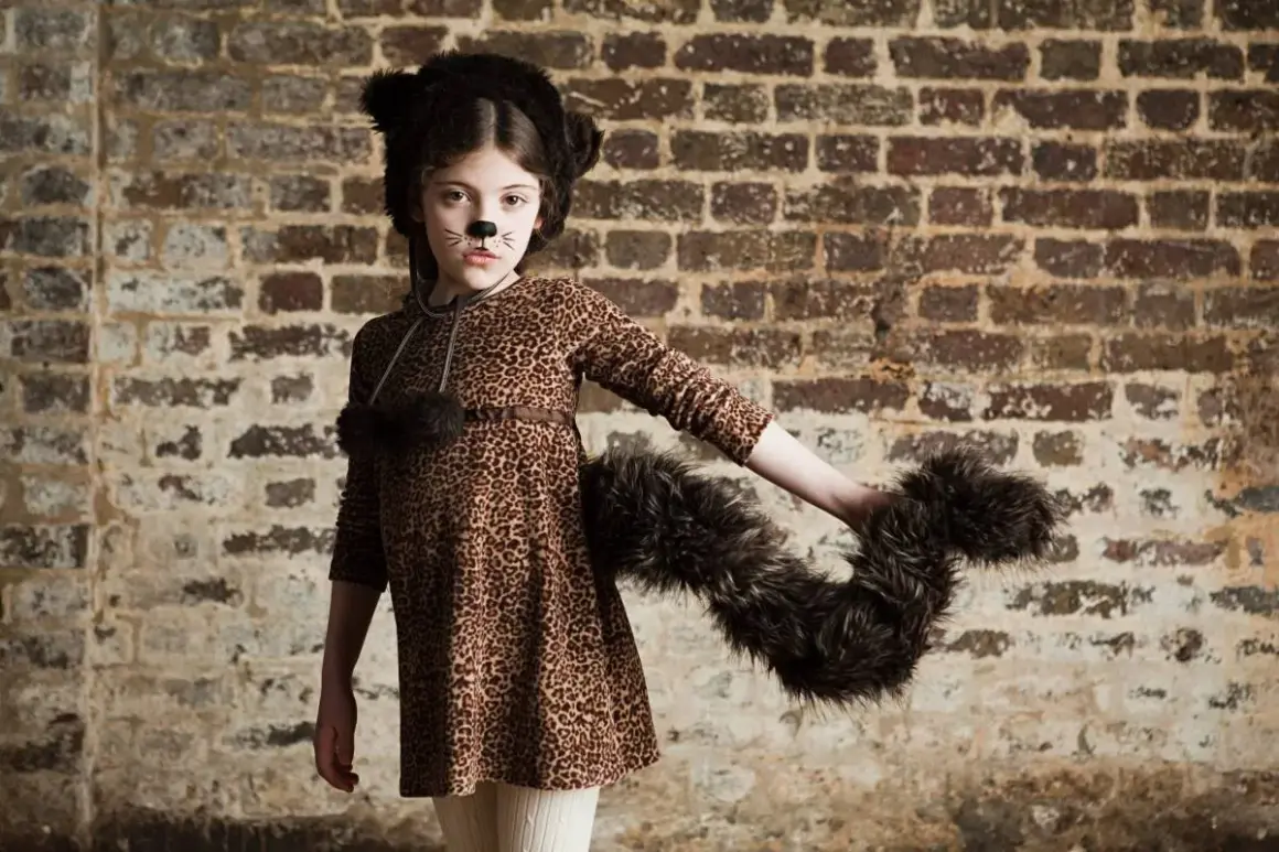 Dziewczynka w stroju kota w butach, z futrzanym ogonem i uszami, gotowa na przygody.