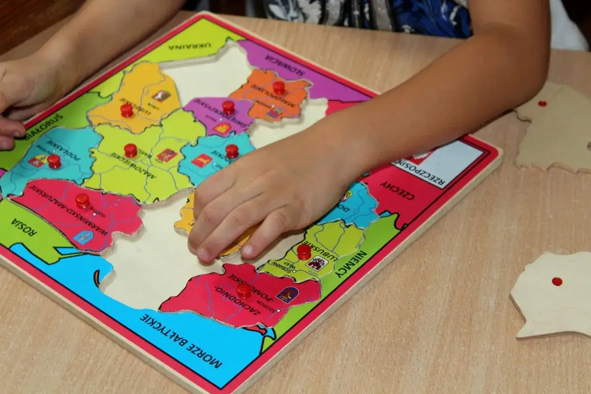 Dziecko układa puzzle z mapą Polski, ćwicząc geografię. To świetne zabawki dla sześciolatków, rozwijające wiedzę i zdolności manualne.