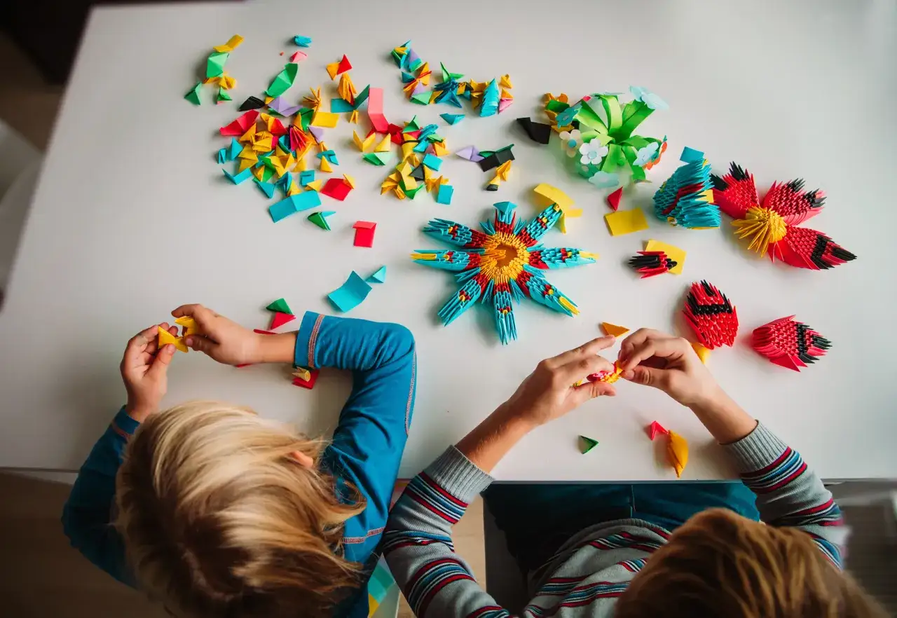 Dzieci tworzą kolorowe origami, rozwijając kreatywne zabawki dla 4 latka. Widać gotowe figurki i mnóstwo małych elementów do składania.