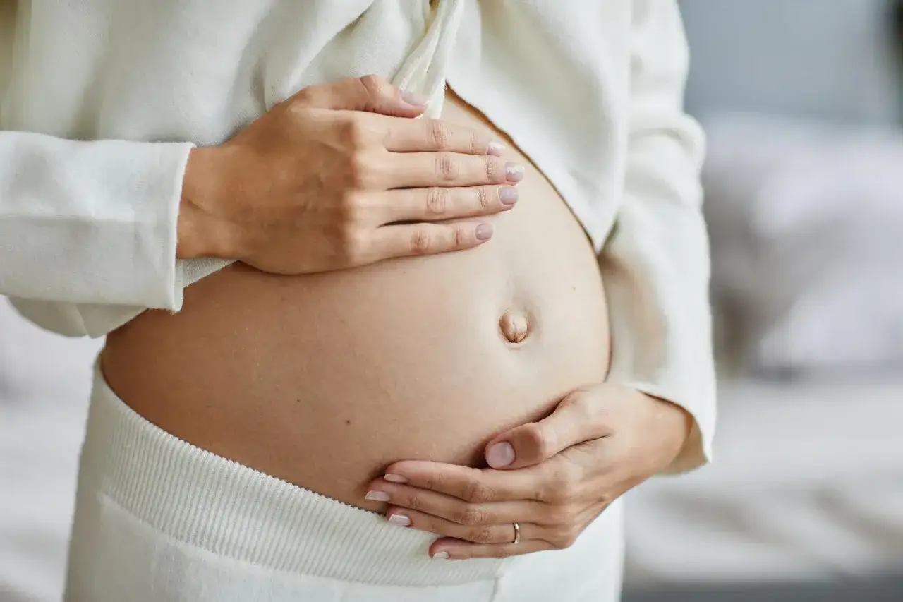 Czułe dłonie na brzuchu, gdy dziecko zaczyna kopać w ciąży. Delikatne ruchy wyczuwalne pod palcami.